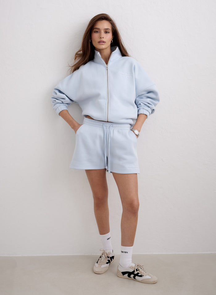 Nainen yllään vaaleansiniset Aura Script Sweat Shorts ja vetoketjullinen huppari merkiltä aim'n. [S-174cm]