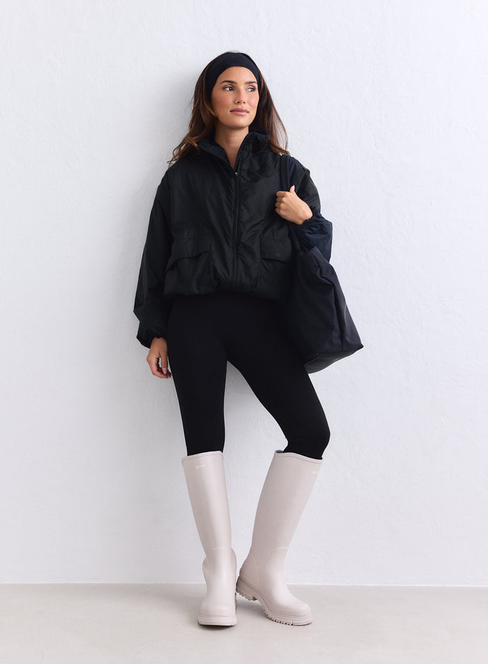Musta aim'n Cloud Jacket naisella, jolla on leggingsit ja korkeat beiget kumisaappaat. [S-163cm]