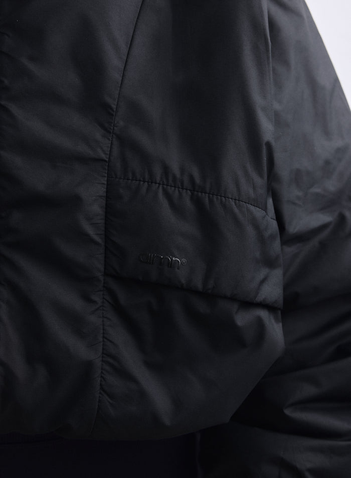 Lähikuva mustasta Cloud Jacket -takista esittelee kudotun kankaan, taskun ja sävysävyisen aim'n-logon. [S-163cm]