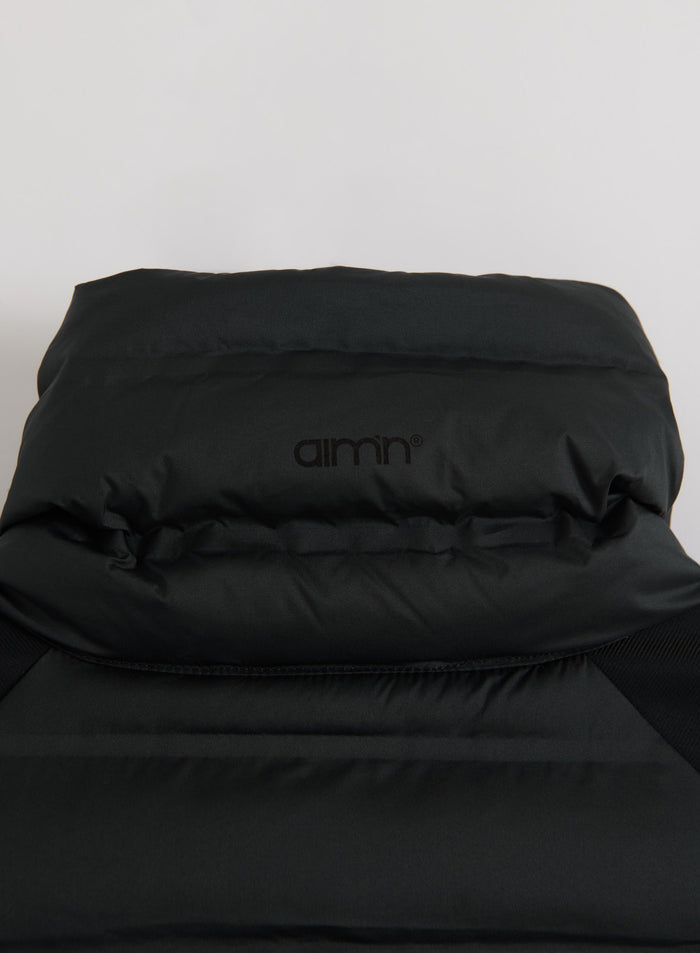 Lähikuva mustasta aim'n Hybrid Jacket -takista tasolle levitettynä, jossa näkyvät topatut osat ja logo