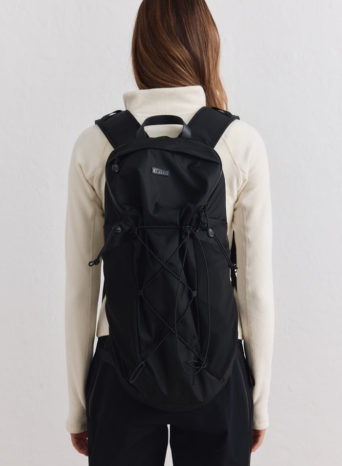 Musta kudottu Outdoor Daypack joustavilla nyöreillä, mallilla kermanvärisessä takissa brändiltä aim'n.