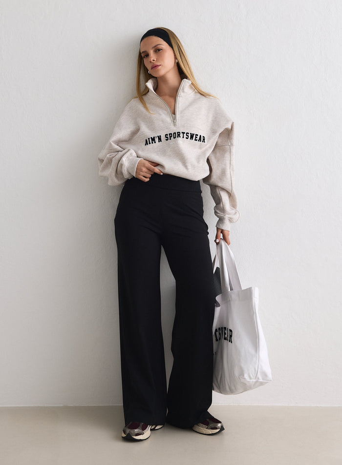Malli, jolla on yllään mustat Black Sense Petite Pants -housut ja beige poolopaita, ja joka pitelee valkoista kangaskassia [M-170cm]