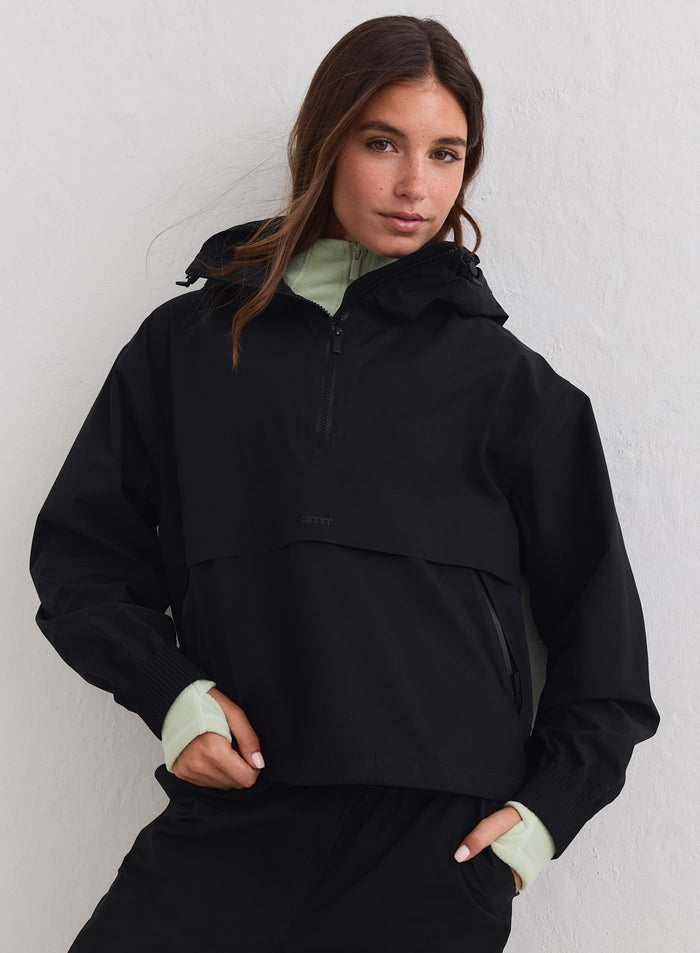 Musta hupullinen aim'n Waterproof Stretch Anorak puolivetoketjulla vaaleanvihreän paidan päällä. [xs-178cm]