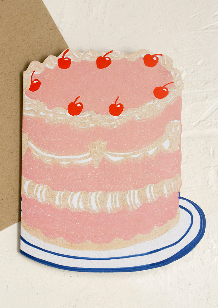 A diecut greeting card in the shape of 3 tier cake with cherries on top.