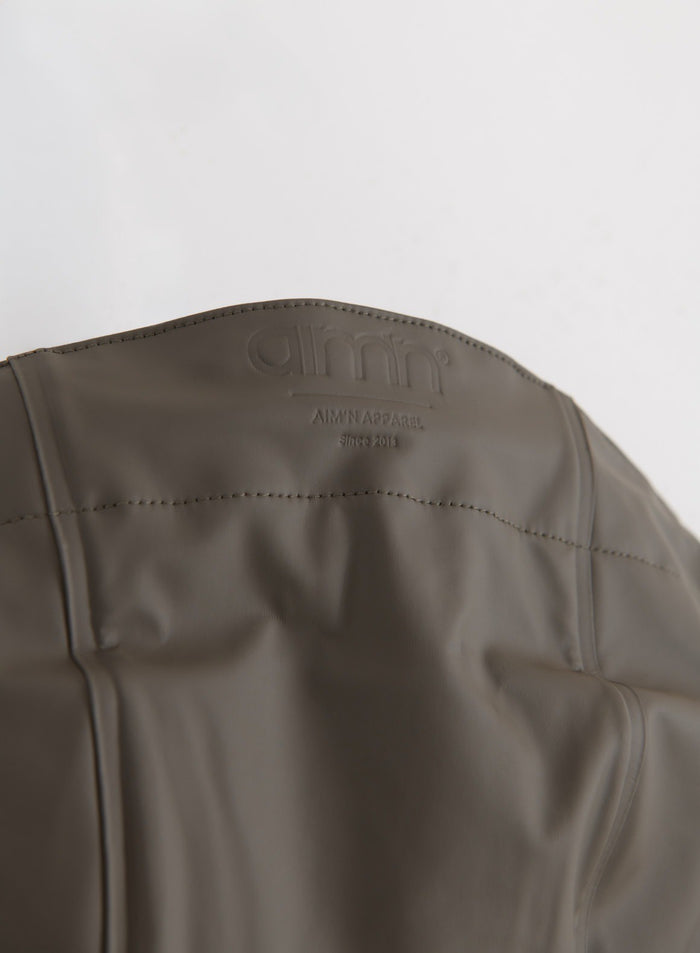 Tasokuvaus Dark Ivy Rain Jacket -sadetakin takaosan kaarrokkeesta ja kohokuvioidusta aim'n-logosta