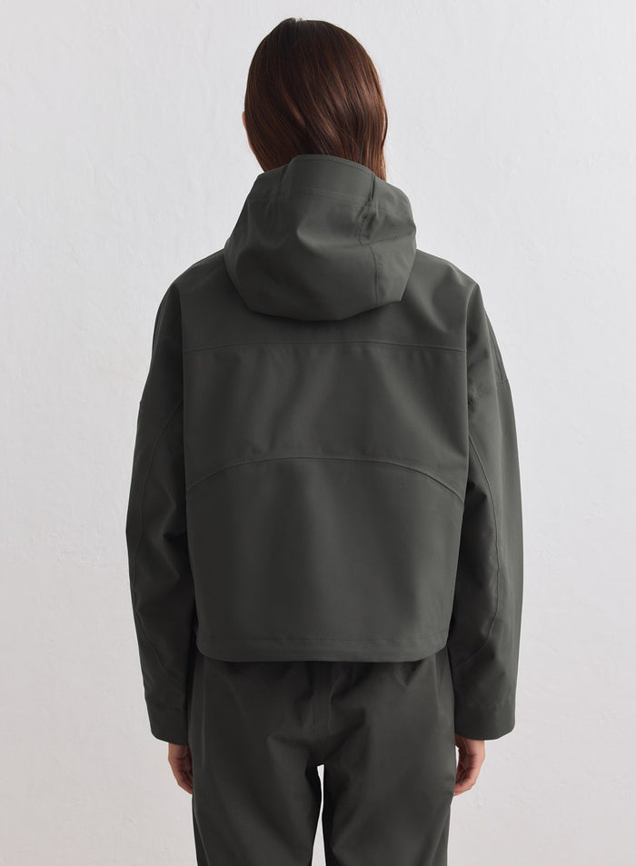 Tummanvihreä kropattu hupullinen Waterproof Jacket merkiltä aim'n kuvattuna takaapäin. [M-178cm]