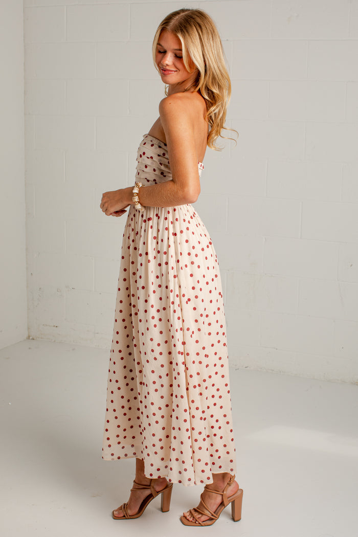 Women's cream strapless midi dress with red polka dots, a fitted bodice and a flowing skirt, styled with strappy heels.
