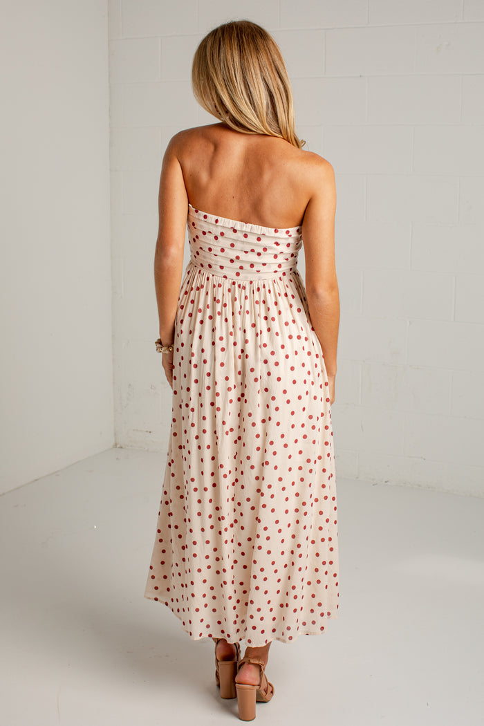 Women's cream strapless midi dress with red polka dots, a fitted bodice and a flowing skirt, styled with strappy heels.
