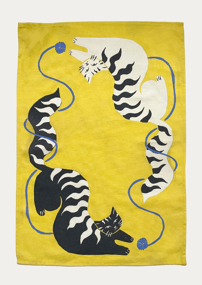 A yellow tea towel with black and white cat pattern