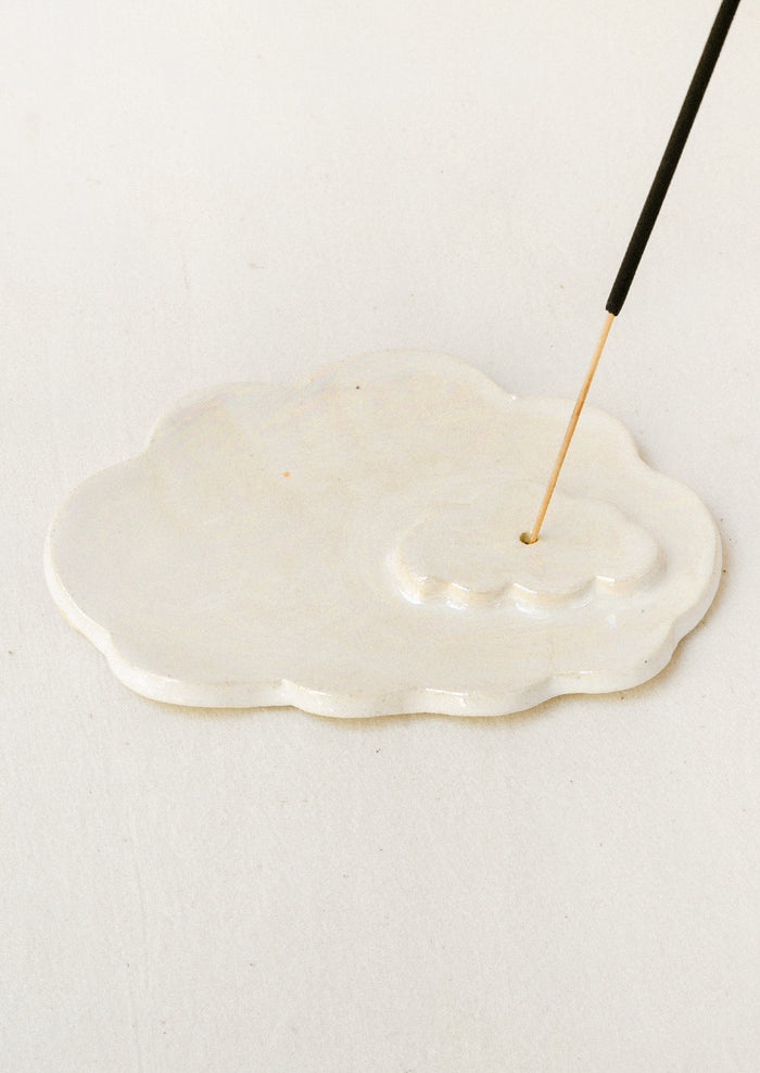 A white ceramic iridescent cloud-shaped incense holder with an incense stick.