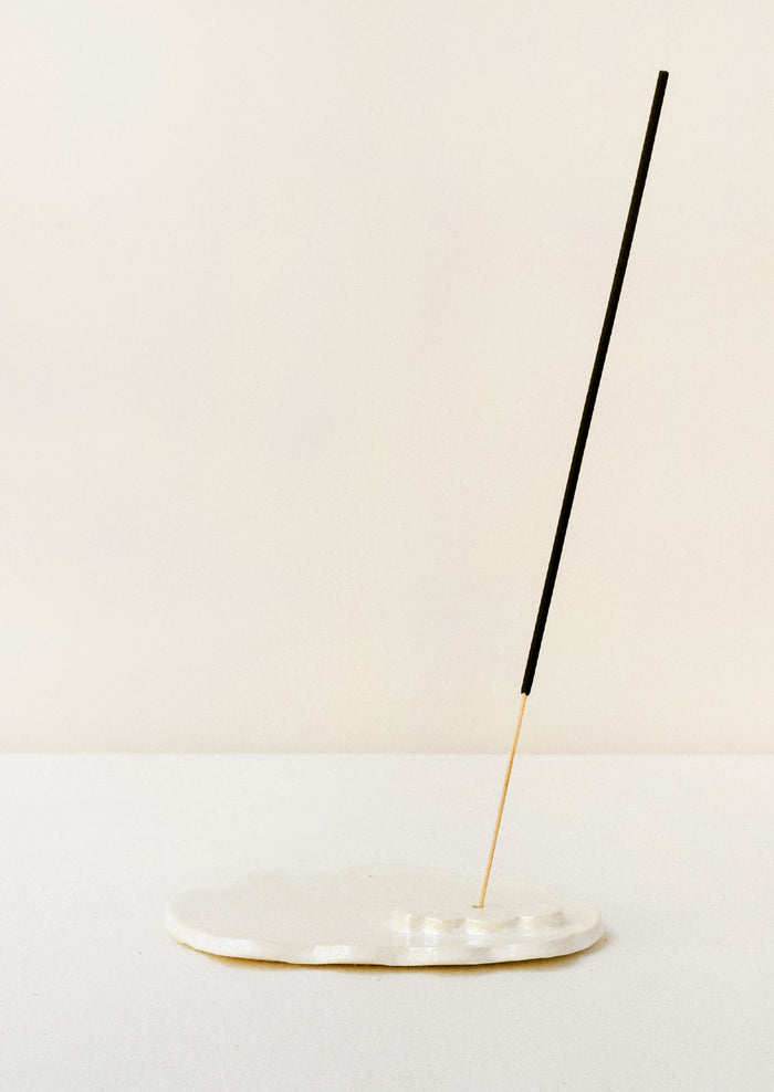 A white ceramic iridescent cloud-shaped incense holder with an incense stick.
