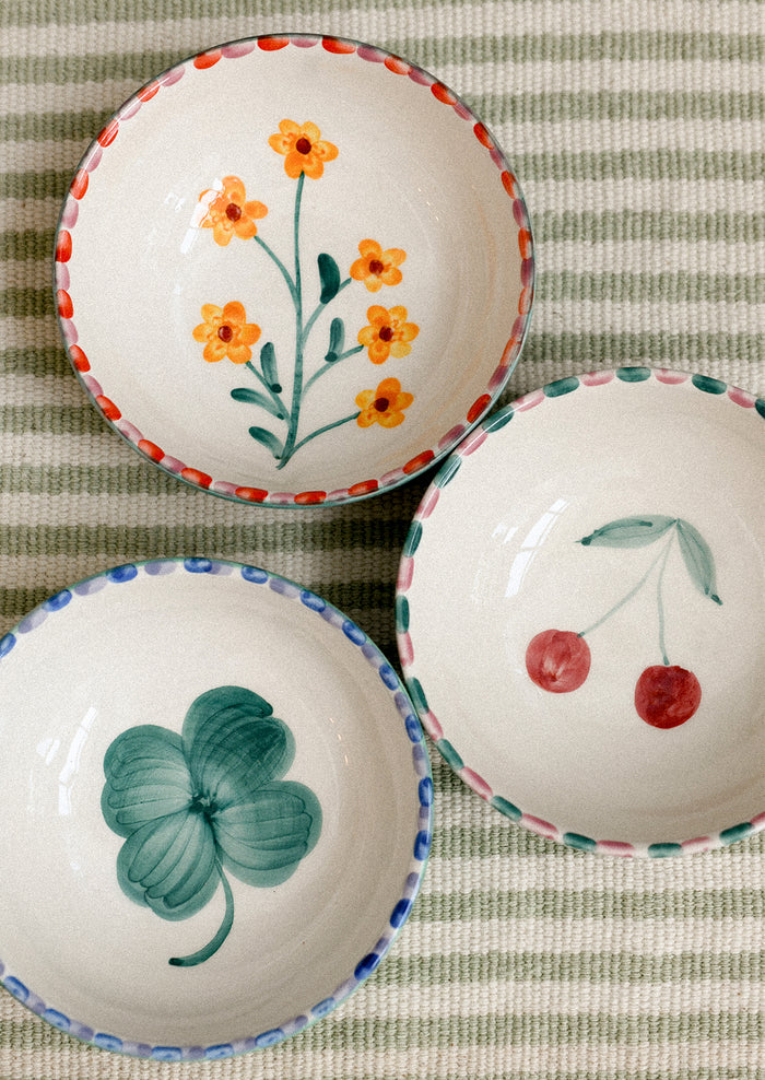 Three small ceramic bowls with floral and fruit designs on a striped fabric background.