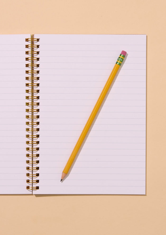 Pencil leaning against an open notebook on a beige background