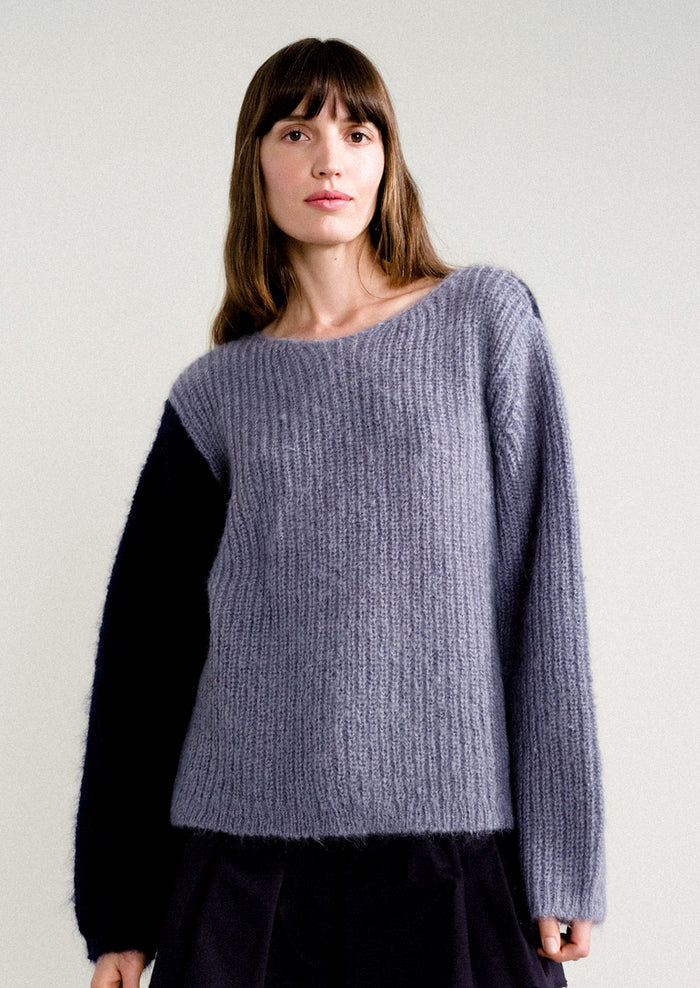 A woman wearing a long sleeve mohair sweater with two-tone colorblocking in dusty blue and navy.