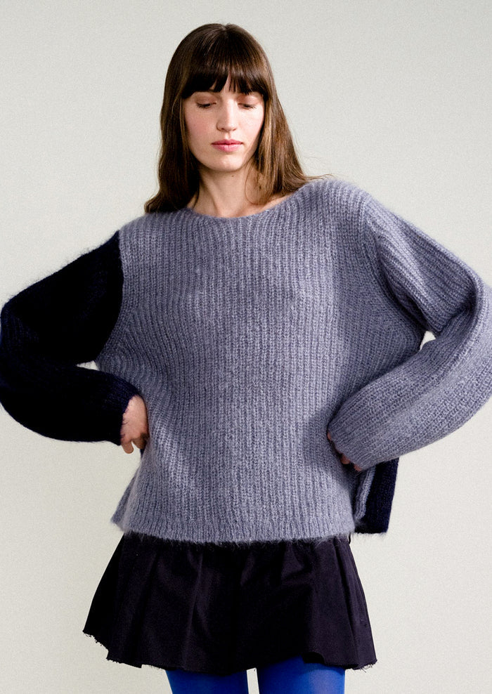 A woman wearing a long sleeve mohair sweater with two-tone colorblocking in dusty blue and navy.