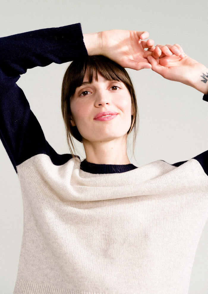 A woman wearing a raglan sweater in light grey and navy.