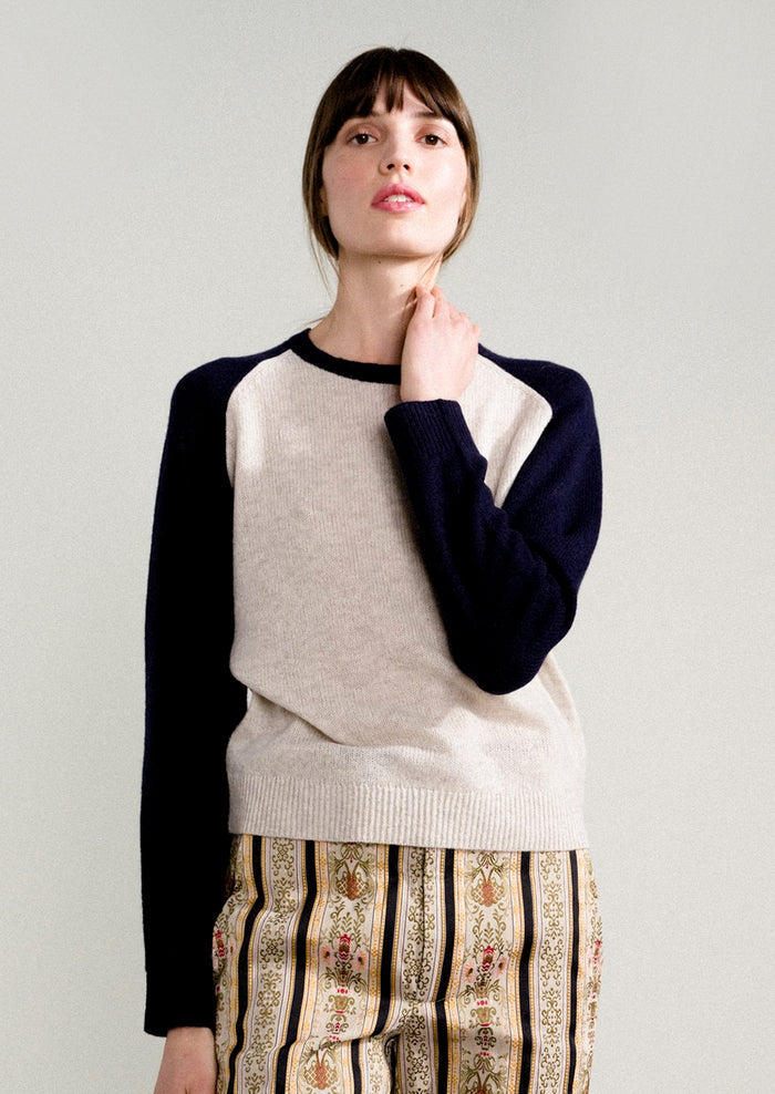 A woman wearing a raglan sweater in light grey and navy.