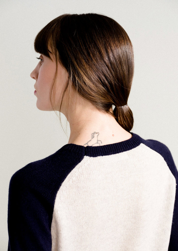 A woman wearing a raglan sweater in light grey and navy.